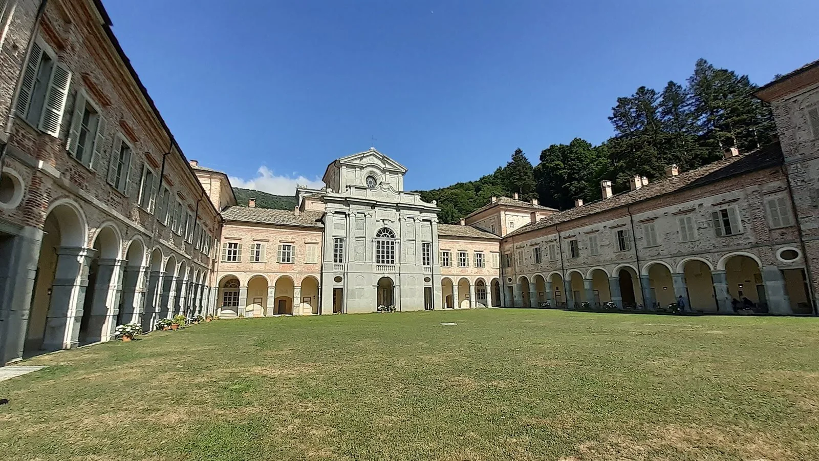 Il grande cortile erboso del Castello di Casotto con i porticati e la facciata della chiesa al centro, circondato dai boschi