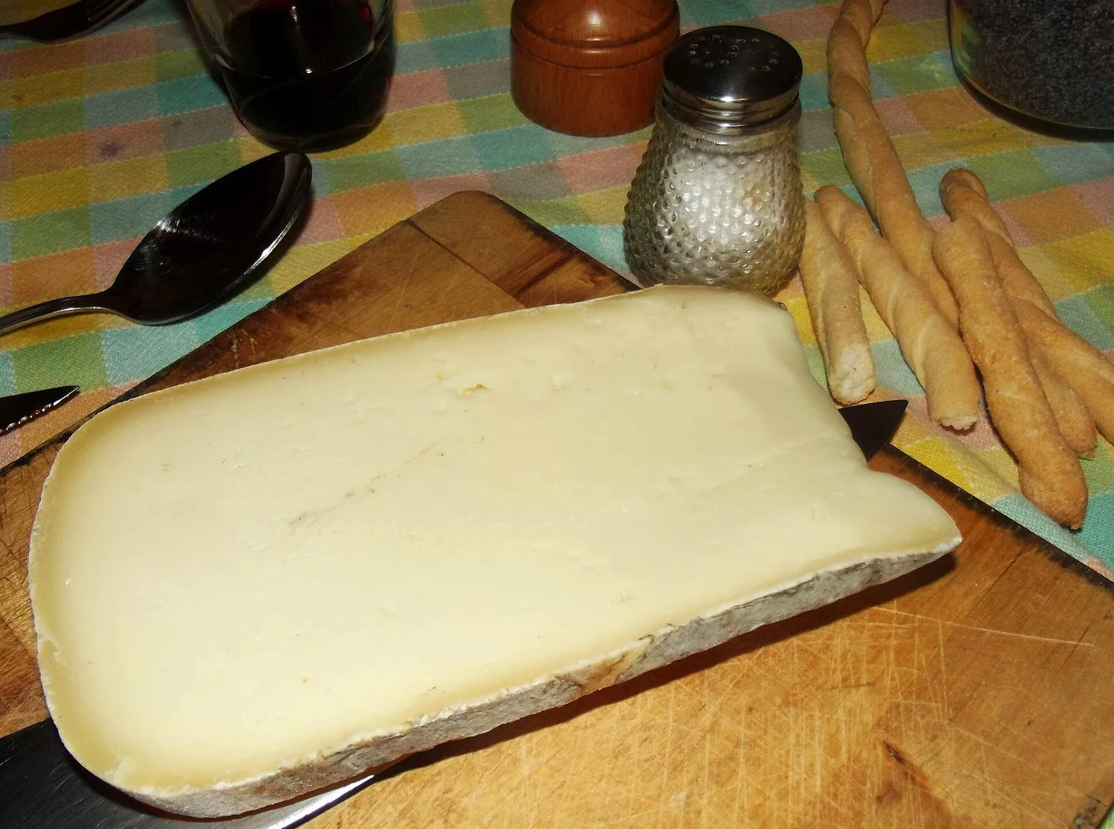 Fetta di formaggio Raschera su un tagliere di legno con grissini e un bicchiere di vino rosso